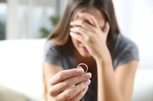 Woman with her face buried in her right hand, holding her wedding ring forward in her left hand